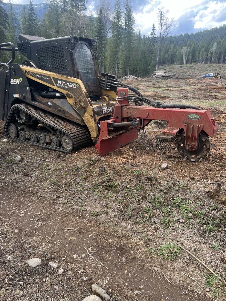 ASV skid steer with Fecon stump grinder attachment in a North Idaho clearing